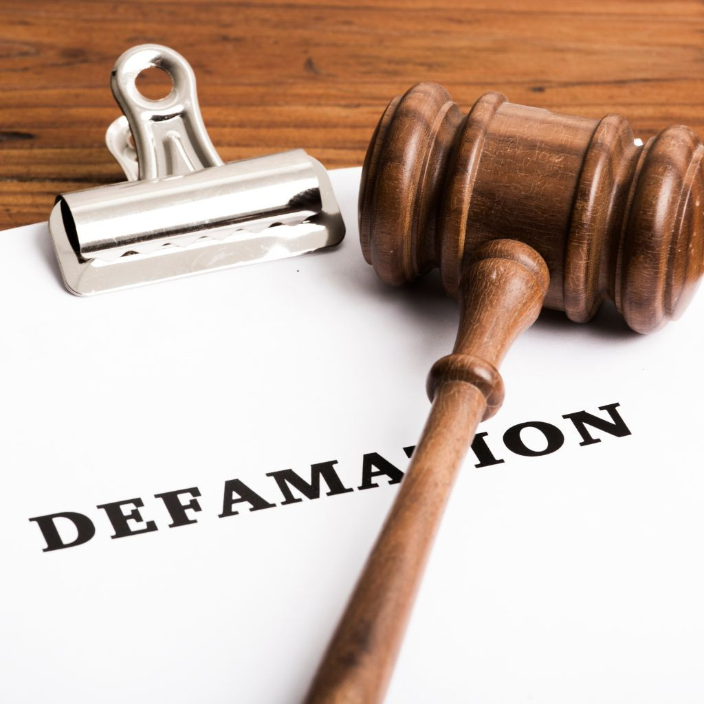 A gavel rests on a document labeled "DEFAMATION," with a metal clip on top, on a wooden surface.